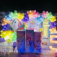 A magical unicorn theme for a 5th birthday. This decoration features a unicorn and rainbow backdrop, a colorful balloon arch, themed plinths, and a large marquee number '5'.