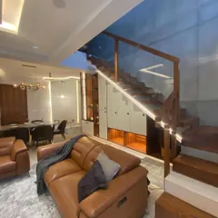 This view showcases the integration of the living area with the wooden staircase. The glass railing maintains an open feel, and the under-stair storage is a practical use of space.