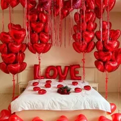 The ultimate romantic gesture with a room full of red heart-shaped foil balloons. The bed is decorated with 'LOVE' foil letters and more hearts, creating an immersive and passionate atmosphere.
