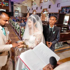 A close-up of the ring exchange during a Catholic ceremony, with the priest guiding the couple. This shot focuses on the symbolic act of commitment.