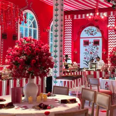 A dining setup from the 'Laal Ishq' theme. The tables are adorned with massive red floral centerpieces in white vases, perfectly complementing the red and white patterned walls and ceiling.