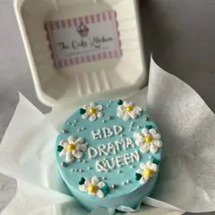 Bento cakes are great for fun and quirky messages. This one, reading "HBD Drama Queen" and decorated with little daisies, is a playful way to celebrate a friend's birthday.