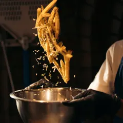 Our truffle fries in action. A chef tosses a batch of crispy fries with truffle oil and parmesan cheese, sending them flying through the air.