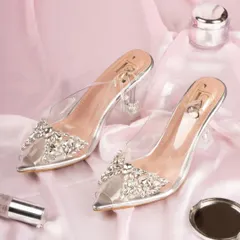 A pair of clear, crystal-embellished heels for Fancy Nancy, styled with beauty products on a pink silk background. This creates a glamorous, feminine, and luxurious feel.