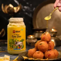 A spoonful of golden ghee is drizzled over a stack of Motichoor Ladoos. The scene is set with diyas and brass plates, creating a warm, festive atmosphere perfect for Diwali.
