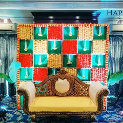 A festive backdrop featuring a checkerboard pattern of red, green, and woven straw panels, with hanging flower tassels. This design is perfect for a baby shower or Haldi ceremony, bringing texture and bright colors to the celebration.