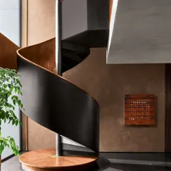 This sculptural spiral staircase, crafted from matte black metal and polished wood, serves as an architectural anchor in the Urban Hearth residence. Its form is designed to create a sense of quiet ascent, turning a functional element into a piece of art.