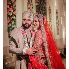A beautiful portrait of the couple on their wedding day. The bride's radiant red lehenga and the groom's elegant sherwani are complemented by the soft floral decor in the background.