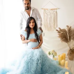 A beautiful portrait of the couple together. She is seated in the flowing blue gown while he stands behind her, both looking towards the camera, ready to welcome their little one.