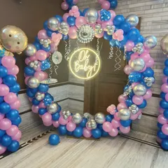 A classic pink and blue baby shower decoration. This setup features a circular balloon arch, an 'Oh Baby' neon sign, and two balloon pillars topped with baby-themed foil balloons.