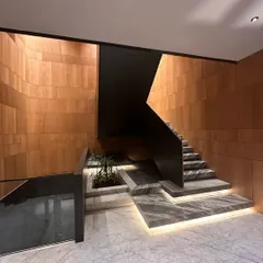 This entrance hall features pristine marble flooring and rich wooden wall panels, with black metal accents framing the space. The staircase is illuminated by integrated LED lights, highlighting the texture of the steps and creating a sophisticated welcome.