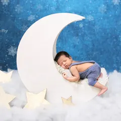 For a touch of magic, I love creating dreamy scenes like this one. Here, a peacefully sleeping baby rests on a crescent moon prop, surrounded by soft clouds and stars. Your baby's safety is always my priority during these creative newborn poses.