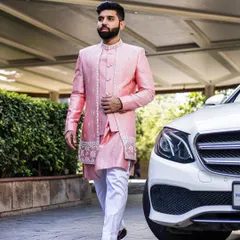 A client looking dapper in a custom pink Indo-Western set. The jacket features an asymmetrical cut with delicate embroidery on the hem and placket, paired with a matching kurta and white trousers for a fresh, modern wedding look.