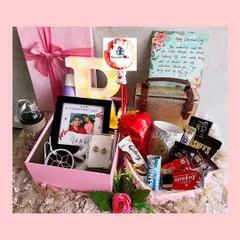 A lavish pink-themed birthday box filled with a variety of gifts, including a handbag, a personalized photo frame, a light-up initial, and an assortment of chocolates and self-care items.