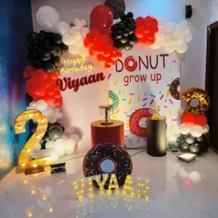 A sweet 'Donut Grow Up' theme for a second birthday. The decor includes a donut-print backdrop, donut-shaped props, and a marquee number '2', all in a fun red, black, and white color scheme.