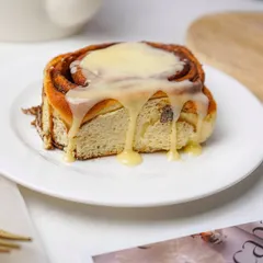 A close-up of a gooey cinnamon roll with cream cheese frosting dripping down the sides, making it look irresistible.