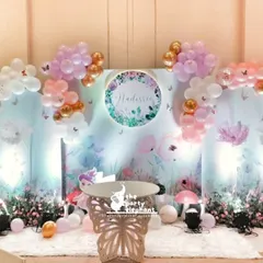A dreamy photo corner for a butterfly-themed baby welcome. The setup features custom-printed backdrops with floral artwork, butterfly-wing props, and soft balloon arrangements in pink, white, and gold.