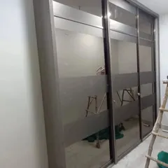 This three-door sliding wardrobe uses frosted glass panels to create a sleek and modern aesthetic, perfect for a minimalist bedroom interior.