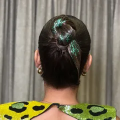 For a modern party look, a touch of glitter can transform a simple bun. This image showcases a sleek, high bun with a green glitter accent, a fun technique I cover for creating eye-catching cocktail hairstyles.