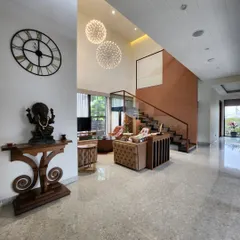 A wide view of a double-height living area that blends modern design with traditional Indian elements, like the carved wooden console and Ganesha statue. The open layout and terrazzo flooring create a bright and welcoming entrance to the home.