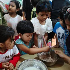 Children take turns mixing the cake batter. This collaborative activity teaches them patience, sharing, and develops hand-eye coordination and strength.