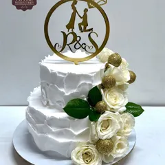 This elegant two-tier engagement cake features a textured white whipped cream frosting and a cascade of fresh white roses with glittery gold balls. A custom topper with the couple's initials adds a personal touch.