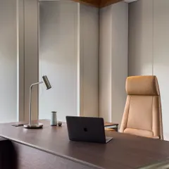 A close-up of the executive desk and ergonomic chair. The clean lines of the desk, minimalist lamp, and high-back leather chair reflect a focus on uncluttered, high-performance workspace design.