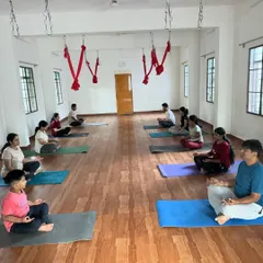 A moment of calm before our 6 am Yin Yoga session begins. Students are centered in Sukhasana (Easy Pose), preparing their minds for the practice ahead. The red hammocks for aerial yoga are visible in the background, showing the variety of classes we offer.