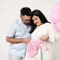 A tender moment as the couple looks at a tiny pink lace outfit for their baby girl. Using baby clothes as props makes the announcement feel so real.