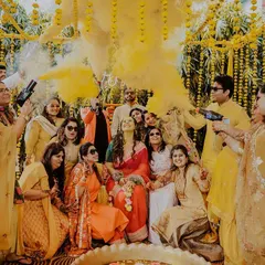 A fun and chaotic group shot from a haldi ceremony. The bride is surrounded by her friends and family as they celebrate with color guns, creating a memorable and high-energy photograph.