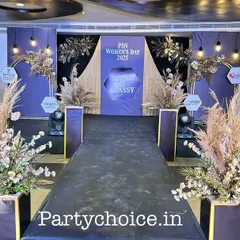 The grand entrance walkway for a corporate celebration. A black carpet runner is flanked by tall planters with pampas grass, leading guests toward the main event area and setting a sophisticated tone.