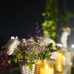 An intimate decor detail showing a basket of flowers placed next to the warm glow of an LED candle, creating a romantic and cozy atmosphere.