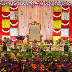 A vibrant and colorful offering display set against a red and yellow backdrop. The foreground is filled with fresh flowers, fruits, and traditional dolls, creating a rich and festive scene.