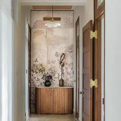 This corridor in Apartment 5026 creates a beautiful vista, drawing the eye towards a feature wall with scenic wallpaper. The reclaimed terrazzo floor and custom wood cabinetry add layers of texture and historical character.