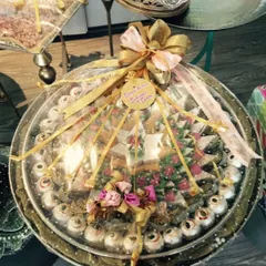 This is an example of a beautifully arranged mithai tray for a wedding. The sweets are artfully placed and wrapped in clear cellophane with a large gold bow, making it a centerpiece of the gift display.