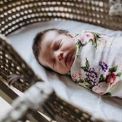 A serene shot of a newborn sleeping peacefully in a bassinet, swaddled in a floral blanket. These classic newborn portraits are timeless.