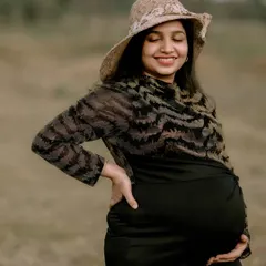 A solo maternity portrait capturing the pure happiness of a mother-to-be. Her joyful smile and the natural, open field setting create a sense of peace and contentment. The simple hat adds a touch of timeless style.