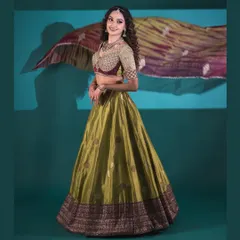 A full view of a custom Banarasi lehenga in a striking olive green. The ensemble features a heavily embroidered blouse with a sweetheart neckline and a flowing skirt, perfect for a sangeet or reception.