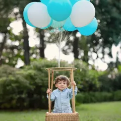 A charming outdoor portrait featuring the popular hot-air balloon prop. The lush green background and bright blue balloons make for a vibrant and cheerful photograph.