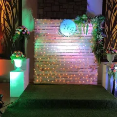 This rustic-chic photo booth is built from a wooden pallet wall and decorated with fairy lights. A custom-designed couple's logo and floral arrangements on either side make it a personal and charming spot for photos.
