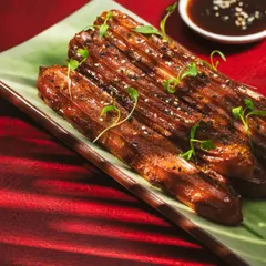 This close up of potato churros from Akina Mumbai uses a rich red background to create a dramatic effect. The lighting is focused on the glossy glaze and sesame seed garnish, making the texture pop.