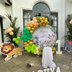 A 'Wild One' jungle safari theme perfect for an outdoor first birthday. This decoration features a custom backdrop with cute safari animals, an organic balloon garland in green and gold, and character cutouts.