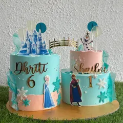 Perfect for sisters, these Frozen-themed twin cakes feature Elsa and Anna in their winter wonderland. We customized the design with each sister's name and age, connecting the two cakes with a delicate bridge.