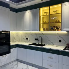 This kitchen showcases a popular two-tone classic design, with bottle green base cabinets and white upper cabinets. The gold handles and marble-patterned floor and backsplash add a touch of opulence.