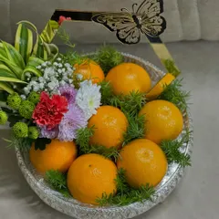 A simple yet elegant fruit tray design. Fresh oranges are nestled in a bed of green foliage within a silver platter, accented with a modern, gold-rimmed butterfly handle for a touch of contemporary style.