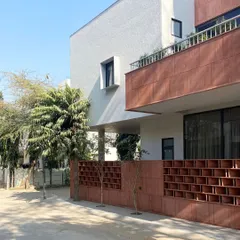 An angled perspective of the Jaipur residence, showing the relationship between the solid upper volume, the open terrace, and the protective jali screen. The design prioritizes both privacy and a connection to the outdoors.