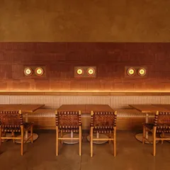The long community seating at Biergarten is set against a wall of textured terracotta tiles. Custom light fixtures, inspired by vintage audio speakers, add a unique, playful detail to the warm and earthy design.