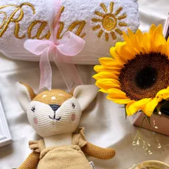A close-up of the personalized 'Raha' towel with a sun embroidered on it, next to the adorable deer plushie and a bright sunflower.