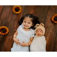 A slightly different angle of the siblings lying on a rustic wood floor surrounded by sunflowers. The sister's proud expression says it all.