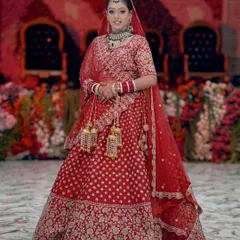 A stunning, classic full-length bridal portrait in a red lehenga, capturing the grandeur and tradition of an Indian wedding.